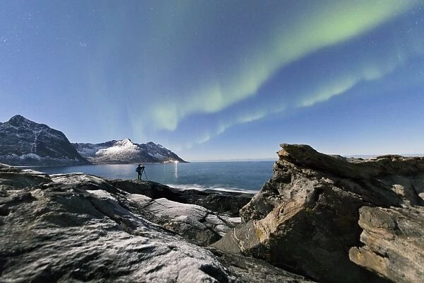 Photographer under the stars and Northern Lights (aurora borealis) surrounded by rocky peaks