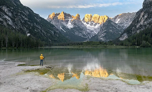 Photographer with tripod admiring the Dolomites at dawn from lake Landro, Dolomites