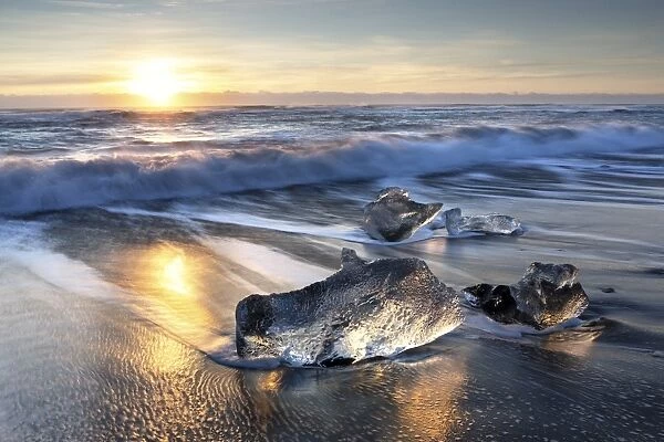 Pieces of glacier ice washed up on black volcanic sand beach at sunrise, near Jokulsarlon