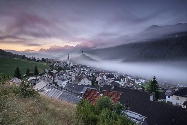 Pink clouds and mist on the village of Ardez at dawn, district of Inn, Lower Engadine