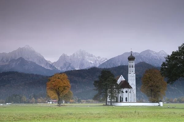 Pink sunrise on St. Coloman Church surrounded by woods and mist of autumn, Schwangau