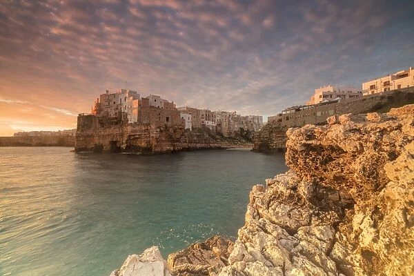 Pink sunrise on the turquoise sea framed by old town perched on the rocks, Polignano a Mare
