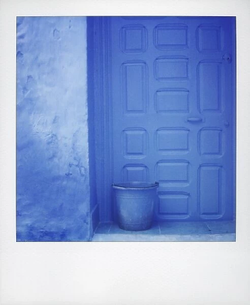 Polaroid of blue plastic bucket against blue door and blue wall