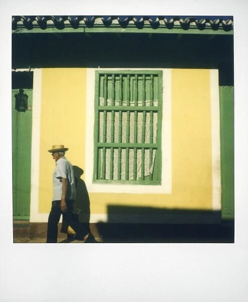 Polaroid of man walking past yellow wall with painted green window grille