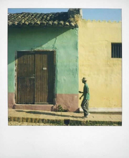 Polaroid of man walking along street against houses painted green and yellow