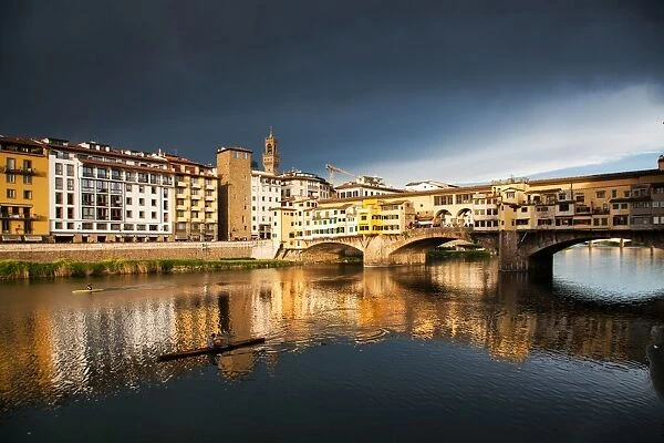 Ponte Vecchio reflected in the Arno River against a dark blue stormy sky, Florence