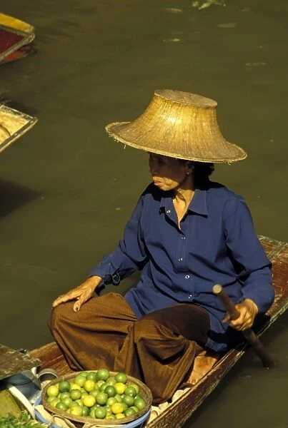 Portrait of a Thai woman vendor in straw hat with a basket of limes