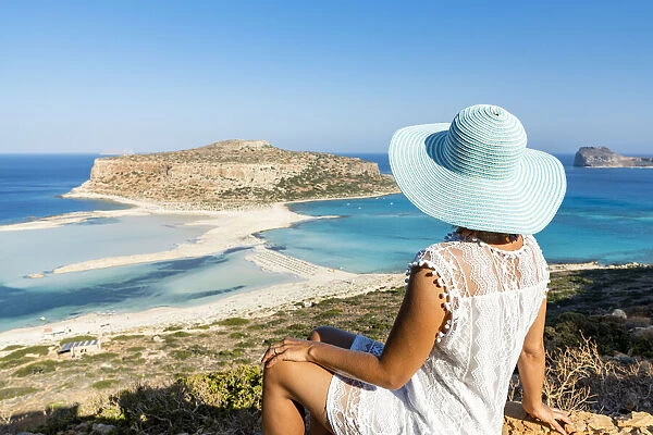 Portrait of woman with hat admiring the idyllic beach and lagoon sitting on top of hill