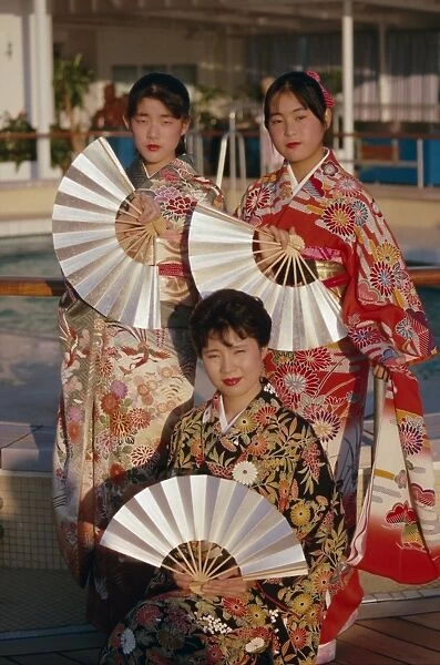 Portrait of three young women in traditional kimonos holding fans