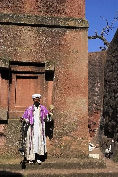 Priest holding cross swings an incense burner at the rock-hewn monolithic church of Bet Giyorgis