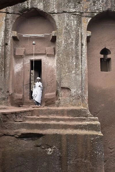 A priest stands at the entrance to the rock-hewn church of Bet Gabriel-Rufael