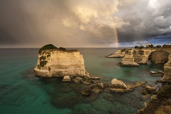 Rainbow frames rocky cliffs known as Faraglioni di Sant andrea surrounded by turquoise sea