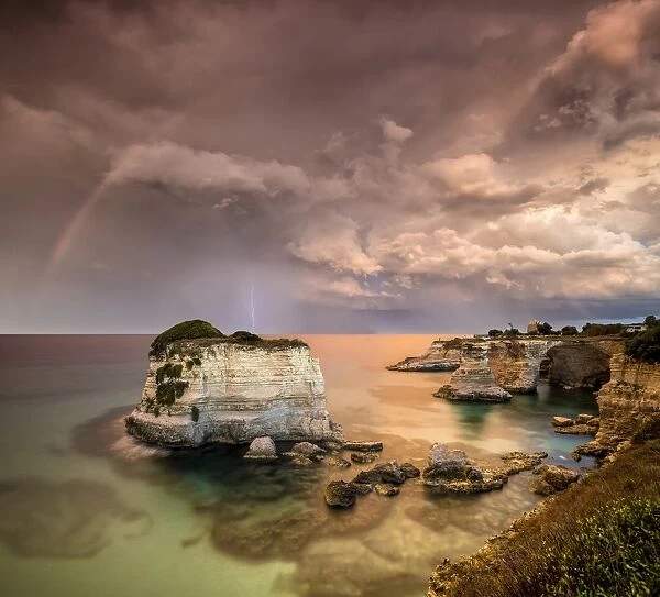 Rainbow and lightning after the storm on cliffs known as Faraglioni di Sant Andrea