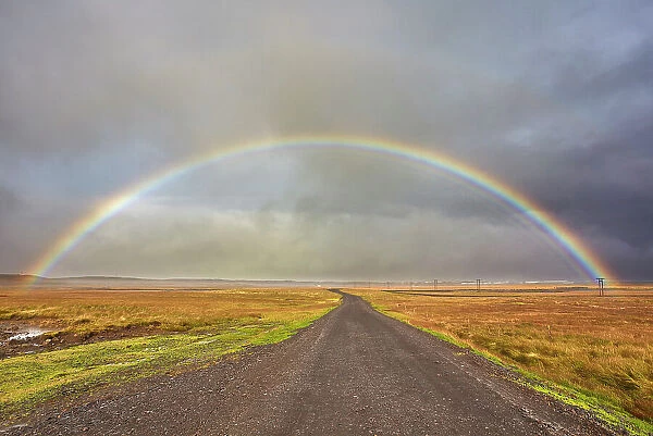 A rainbow straddles a road in countryside near Rif, Snaefellsnes peninsula, western Iceland, Polar Regions
