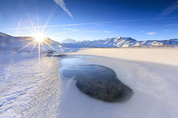 Rays of sun on the frozen Lake, Piz Umbrail framed by Mount Ortles in background