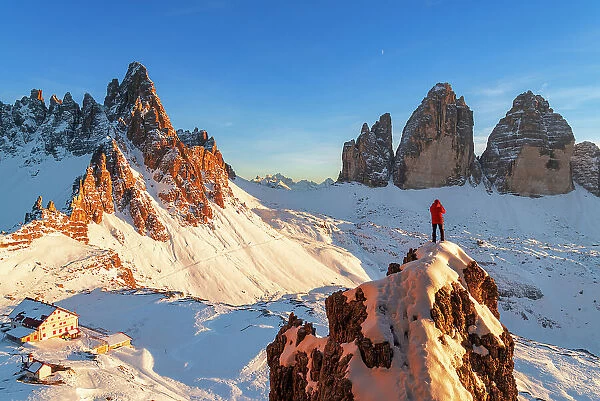 Rear view of a hiker admiring Tre Cime di Lavaredo (Lavaredo Peaks) (Drei Zinnen) from the top of a giant rock, winter view, Sesto (Sexten), Dolomites, South Tyrol, Italy, Europe