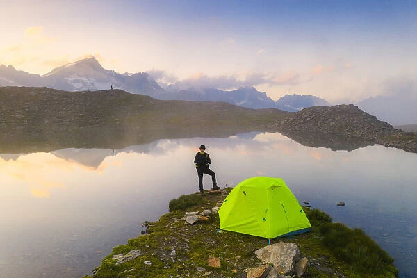 Rear view of man with hat standing outside tent at Obere Schwarziseeli lake at dawn
