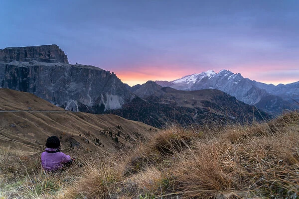 Rear view of woman sitting on grass admiring sunrise on Marmolada and Sass Pordoi