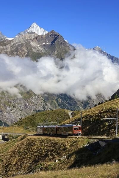 The red Bahn train proceeds with the peak of Dent Herens in the background, Gornergrat