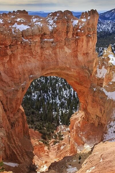 Red-hued limestone arch lit by morning sun with snow in winter at Natural Bridge, Bryce Canyon National Park, Utah, United States of America, North America