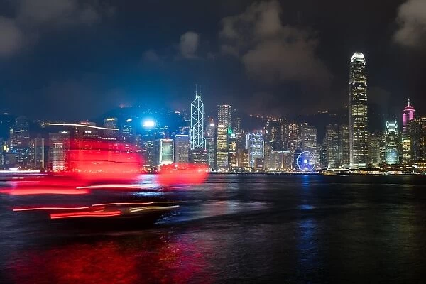 A red junk sailboat glides in front of the Hong Kong skyline at night, Hong Kong