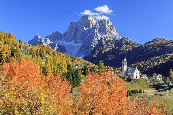 Red and orange trees with the tiny church of Selva di Cadore, in the Dolomites, with Mount Pelmo in the background, Veneto, Italy, Europe