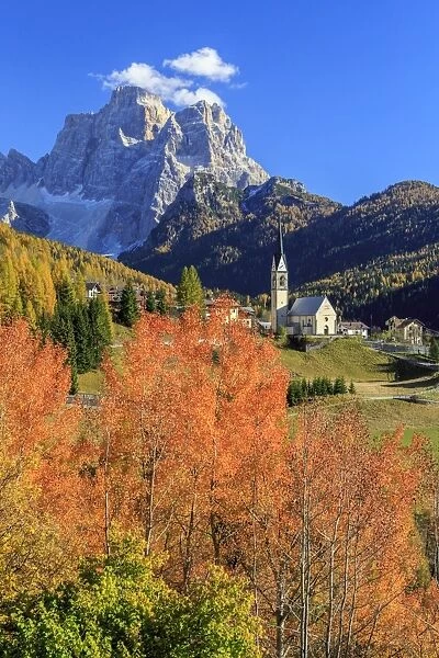 Red and orange trees in front of the tiny church of Selva di Cadore, in the Dolomites, with Mount Pelmo in the background, Veneto, Italy, Europe