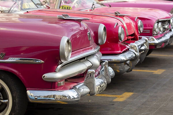 Red and pink vintage American car taxis on street in Havana, Cuba, West Indies, Central America