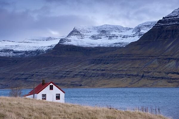 Red-roofed house and snow-capped mountains in Reydarfjordur fjord, East Fjords