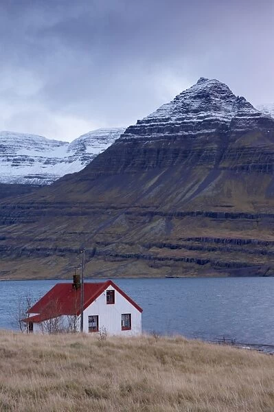Red-roofed house and snow-capped mountains in Reydarfjordur fjord, East Fjords