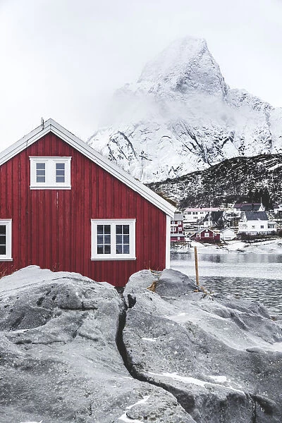 Red Rorbu in the frozen landscape with snowcapped Olstind mountain in the background, Reine, Nordland, Lofoten Islands, Norway, Scandinavia, Europe