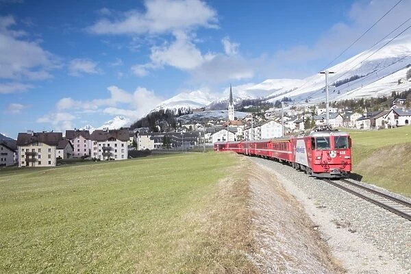 The red train runs across the alpine village of Zuoz in spring, Maloja, Canton of Graubunden