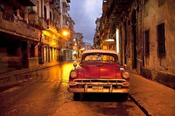 Red vintage American car parked on a floodlit street in Havana Centro at night, Havana, Cuba, West Indies, Central America
