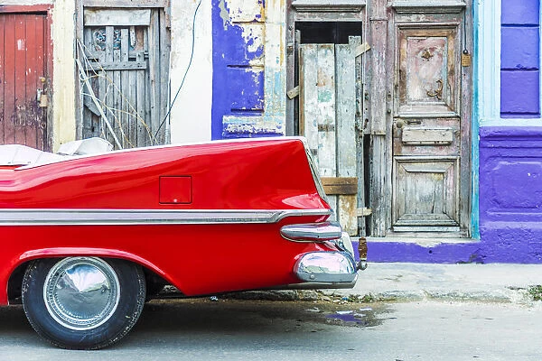A red vintage car parked against colourful local architecture in Havana, Cuba, West Indies