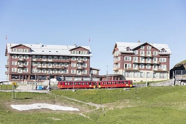 Red wagons of Wengernalpbahn rack railway run next to alpine hotels, Wengen, Bernese Oberland