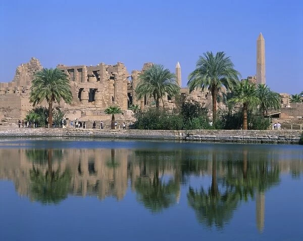 Reflections in the sacred lake of the temple, obelisks and palm trees at Karnak