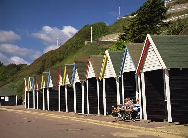 Relaxing on the Promenade outside a colourful beach hut below the cliff in early summer sunshine