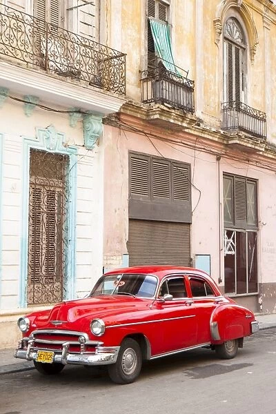 Restrored red American car pakred outside faded Colonial buildings, Havana