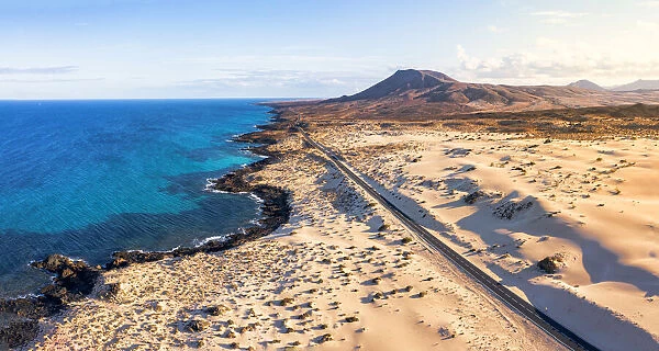 Empty road crossing the sand dunes overlooking the ocean, Corralejo Natural Park
