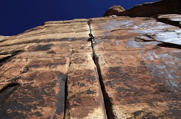 A rock climber tackles an overhanging crack in a sandstone wall on the cliffs of Indian Creek