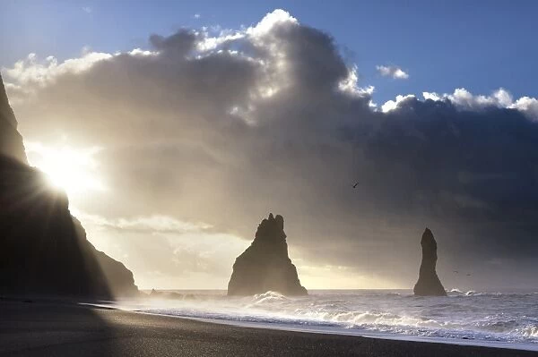 Rock stacks of Reynisdrangar in silhouette at sunrise, from Halsanefs Hellir Beach