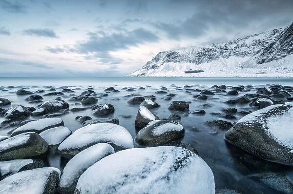 Rocks in the cold sea and snow capped mountains under the blue light of dusk, Unstad