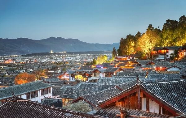 The roofs of Lijiang Dayan, UNESCO World Heritage Site, with illuminated trees of Lion Hill at blue hour as seen from an elevated point of view, Yunnan, China, Asia
