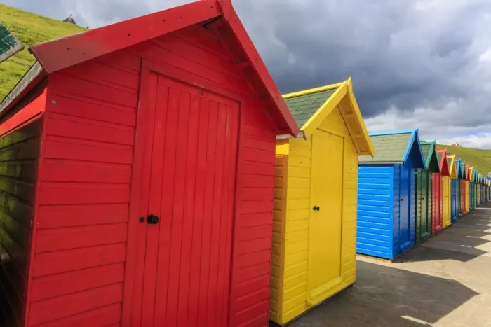 Framed Print : Row of colourful beach huts and their shadows, with grassy cliffs, West Cliff Beach Framed Print : Row of colourful beach huts and their shadows, with grassy cliffs, West Cliff Beach