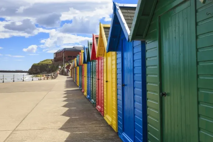 Framed Print : Row of colourful beach huts and their shadows, distant surfers in sea, West Cliff Beach Framed Print : Row of colourful beach huts and their shadows, distant surfers in sea, West Cliff Beach