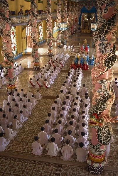 Rows of monks at prayer inside a temple of the Caodai religious sect