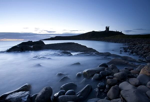 The ruins of Dunstanburgh Castle at dawn with Greymare Rock partly sumberged