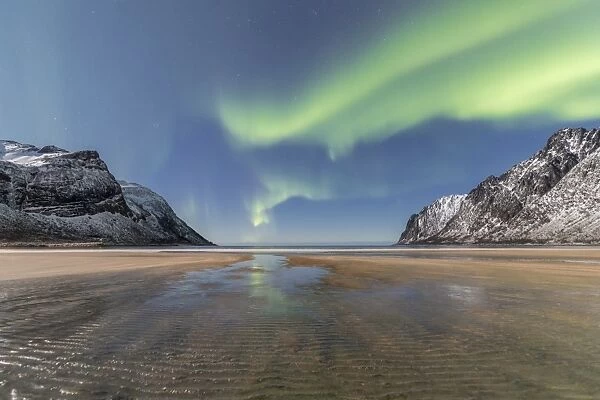Sandy beach and snowy peaks framed by the Northern Lights (aurora borealis) in the polar night