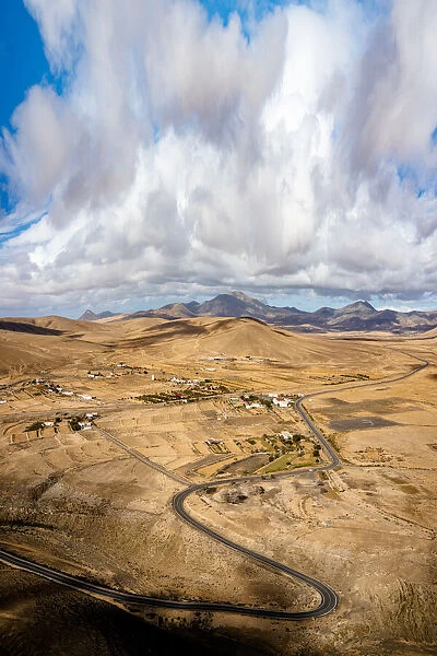 Scenic clouds on winding road running through desert mountains, aerial view, Tefia