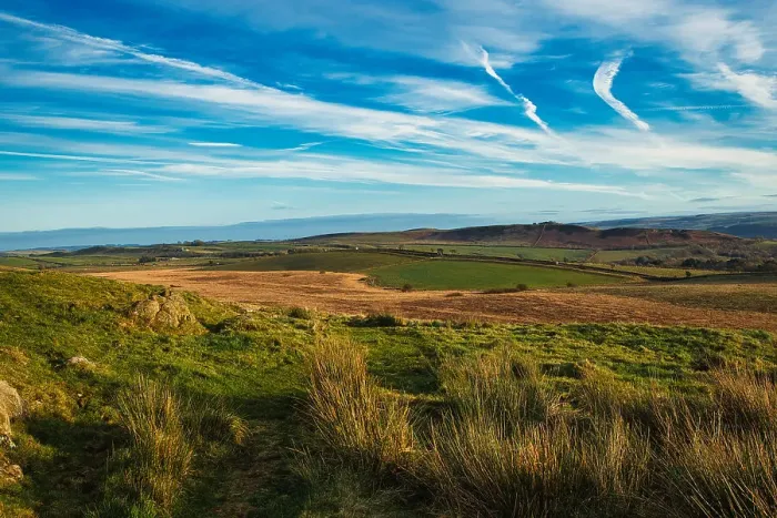 Framed Print : Scenic landscape with lush green fields, rolling hills, and a clear blue sky with wispy clouds at Sycamore Gap, Northumberland, UK